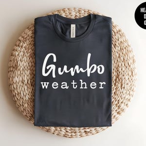 May include: A dark heather grey t-shirt with the text "Gumbo weather" printed in white.