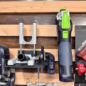 May include: A collection of power tools mounted on a wooden wall. The tools include a black and green oscillating multi-tool with the text "STARLOCK MAX", a gray and black tool with a U-shaped support, and other black and gray tools.