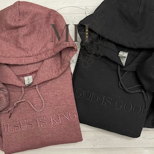 May include: Two hooded sweatshirts, one in a maroon color with the text "JESUS IS KING" and the other in black with the text "GOD IS GOOD".