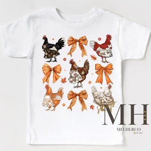 May include: White t-shirt featuring a colorful graphic of chickens wearing aprons and bows. The design includes orange bows and autumn leaves. The text "MH MELHERCO EST 2020" is printed on the bottom right.