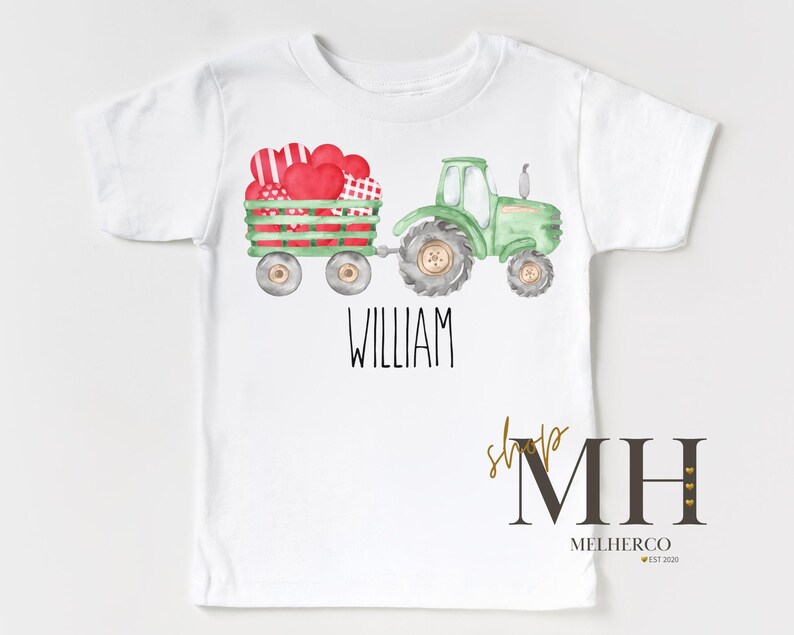 May include: White t-shirt with a watercolour illustration of a green tractor pulling a wagon filled with red and patterned hearts. The name "WILLIAM" is printed in black. The shop logo "MH" is in the bottom right corner.