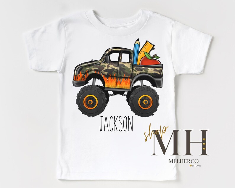 K&ouml;nnte beinhalten: Wei&szlig;es T-Shirt mit einem Monster-Truck-Design. Der Truck hat eine Tarnkabine und Flammen. Ein Bleistift, ein Lineal und ein Apfel befinden sich in der Ladefl&auml;che. Der Name "JACKSON" ist darunter gedruckt.