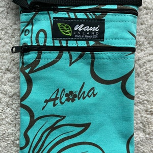 May include: A turquoise fabric pouch with a black zipper closure and a black strap. The pouch features a brown floral pattern and the word "Aloha" in script. The label reads "Maui Island made in Hawaii USA."