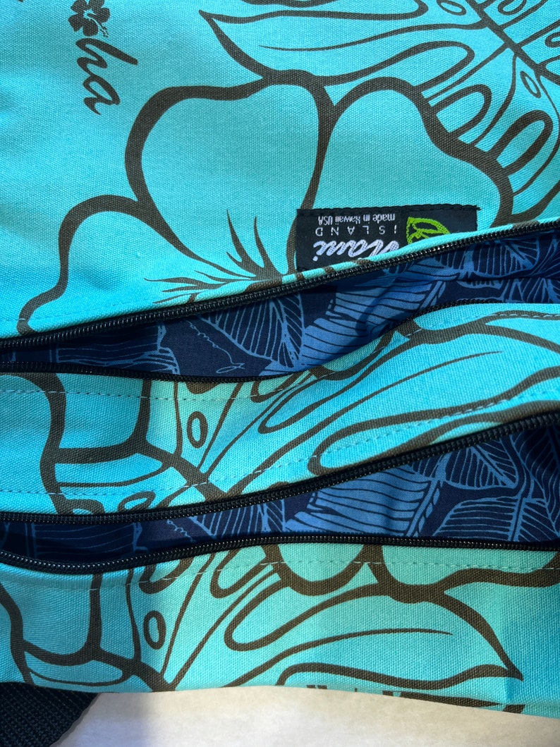 May include: A blue and black patterned tote bag with a zipper closure. The bag has a label that reads "Island Soul! Made in Hawaii, USA".