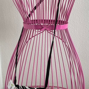 May include: A black and white crossbody bag with a floral design and the word "Hawaii" printed on it. The bag has a black strap and is displayed on a pink wireframe mannequin.