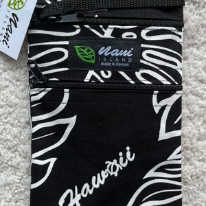 May include: Black and white patterned travel pouch with three zippered compartments. The pouch features a floral design and the word "Hawaii" in white script. A tag reads "Maui Island made in Hawaii".