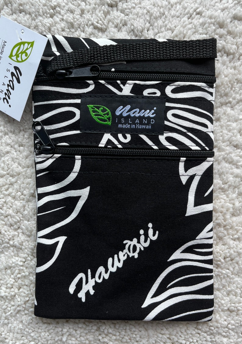 May include: Black and white patterned travel pouch with three zippered compartments. The pouch features a floral design and the word "Hawaii" in white script. A tag reads "Maui Island made in Hawaii".