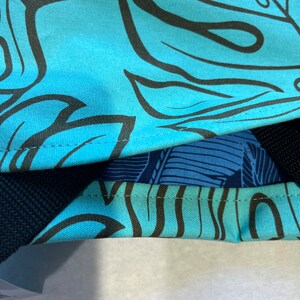 May include: A blue canvas tote bag with a black and white tropical leaf pattern. The bag has a black strap and a blue and white patterned lining.