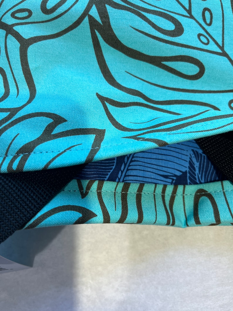 May include: A blue canvas tote bag with a black and white tropical leaf pattern. The bag has a black strap and a blue and white patterned lining.