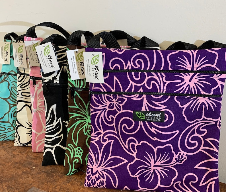 May include: A set of eight zippered pouches with floral patterns. The pouches are made of fabric and have a black zipper. The pouches are lined up in a row, with the largest pouch at the back and the smallest pouch at the front. The pouches are all different colors, including purple, pink, black, green, and white. The pouches have the text "Maui Island" printed on them.
