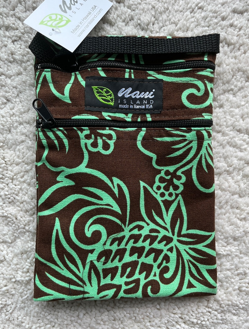 May include: A brown and mint green crossbody bag with a floral pattern. The bag has a black strap and two zippered compartments. The tag reads "Nani Island made in Hawaii USA".