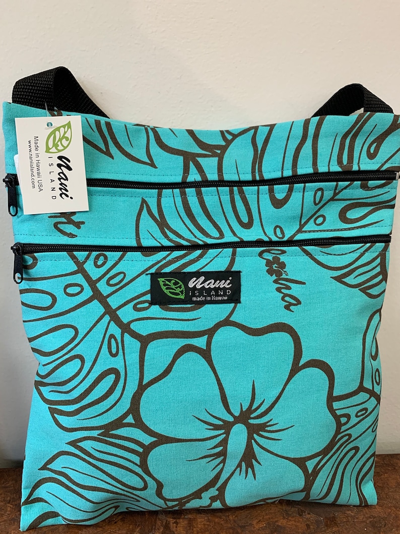 May include: A turquoise blue zippered pouch with a brown floral print. The pouch has a black strap and a label that reads "Maui Island Made in Hawaii www.mauisland.com".
