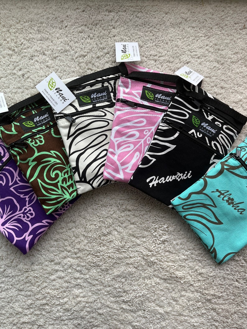 May include: A collection of colorful, patterned pouches with zippers. Designs include floral and leaf motifs in purple, brown, white, pink, black, and teal. Each pouch has a black strap and a tag that reads "Maui Island". The word "Hawaii" is printed on one pouch.