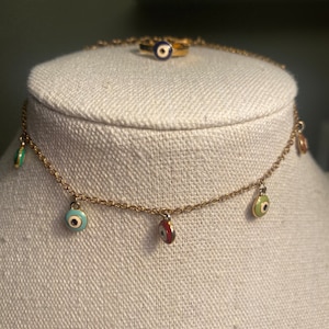 May include: A gold chain necklace with five small, colorful evil eye charms. The charms are blue, green, red, and white.