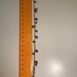 K&ouml;nnte beinhalten: Silberfarbenes Fu&szlig;kettchen mit kleinen Anh&auml;ngern, darunter Herzen, Perlen und sch&auml;delartige Anh&auml;nger. Das Fu&szlig;kettchen ist etwa 20 cm lang. Die Anh&auml;nger sind eine Mischung aus Silber und Dunkelrot.