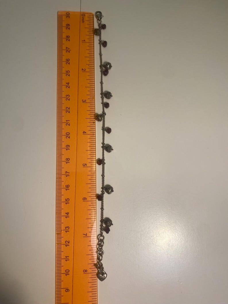 K&ouml;nnte beinhalten: Silberfarbenes Fu&szlig;kettchen mit kleinen Anh&auml;ngern, darunter Herzen, Perlen und sch&auml;delartige Anh&auml;nger. Das Fu&szlig;kettchen ist etwa 20 cm lang. Die Anh&auml;nger sind eine Mischung aus Silber und Dunkelrot.