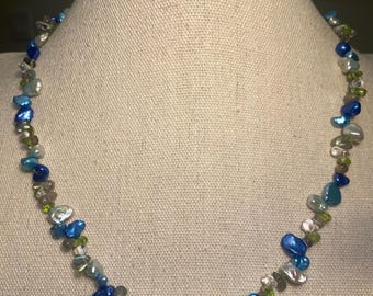 May include: A necklace made of blue, green and white stones. The stones are irregular in shape and size, and they are strung together on a silver chain.