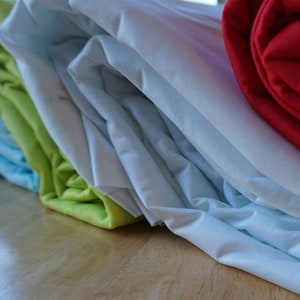 May include: A stack of four fabric swatches in different colors and textures. The top swatch is red, the second is white, the third is green, and the bottom is light blue.