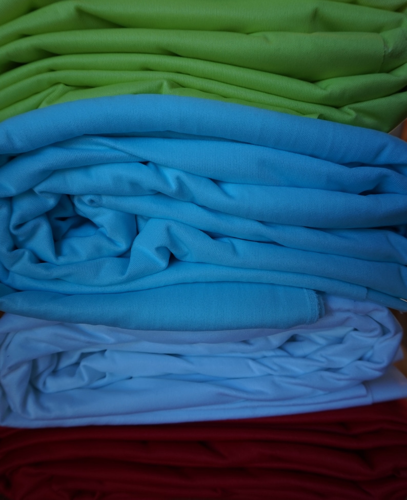 May include: A stack of fabric in four colors: green, blue, white, and red. The fabric is folded neatly and the colors are vibrant.