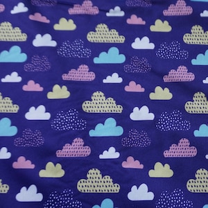 May include: Purple fabric with a repeating pattern of white, yellow, pink, and blue clouds. The clouds have a variety of patterns, including polka dots, stripes, and dashes.