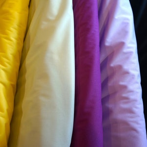 May include: Five rolls of fabric in different colors: yellow, white, purple, lavender, and black.