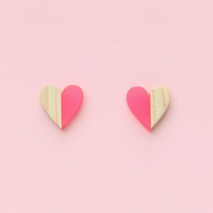 May include: A pair of pink and wood heart-shaped earrings. The earrings are half pink and half wood.