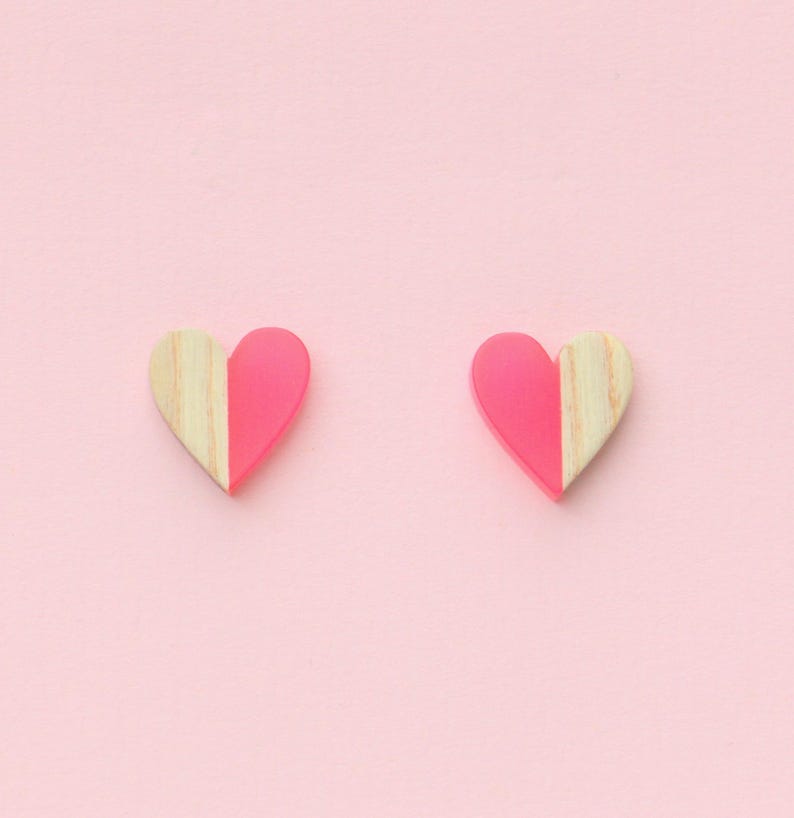 May include: A pair of pink and wood heart-shaped earrings. The earrings are half pink and half wood.
