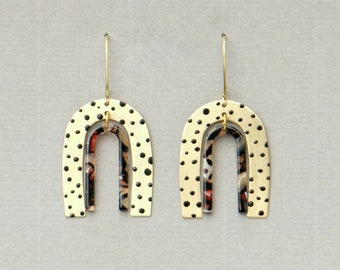 May include: A pair of gold earrings with a black and white polka dot pattern and a layered design. The earrings are shaped like arches.