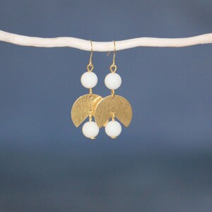 May include: Gold earrings with white beads and a crescent moon design.