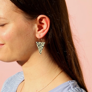 Könnte beinhalten: Ein Paar dreieckige Ohrringe mit einem schwarz-weißen Tupfenmuster. Die Ohrringe sind aus cremefarbenem Material gefertigt und haben einen goldenen Ring.