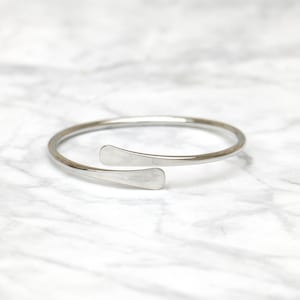Può includere: Un braccialetto rigido in argento con un design semplice e aperto. Il braccialetto è realizzato in un unico pezzo continuo di metallo piegato a forma di cerchio. Le estremità del braccialetto sono unite da un piccolo pezzo di metallo piatto.