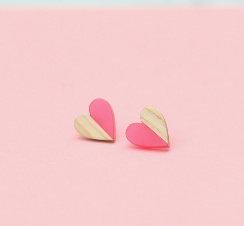 May include: A pair of pink and wood heart-shaped earrings. The earrings are half pink and half wood.