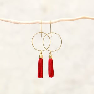 May include: Gold hoop earrings with red tassel charms.
