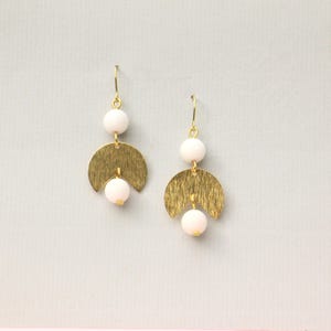 May include: A pair of gold earrings with white beads and a textured, crescent moon design.