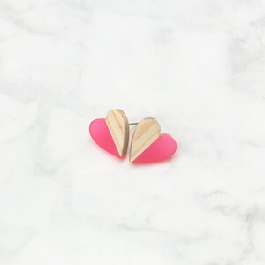 May include: A pair of pink and wood heart-shaped earrings. The earrings are made of acrylic and wood and have a simple, modern design.