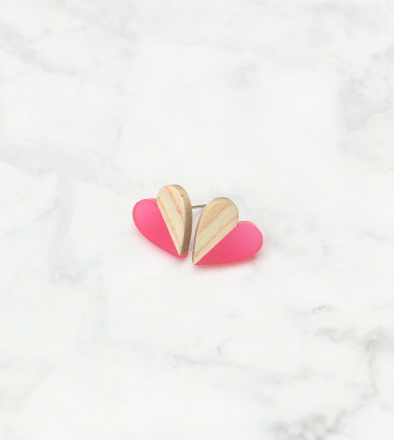 May include: A pair of pink and wood heart-shaped earrings. The earrings are made of acrylic and wood and have a simple, modern design.