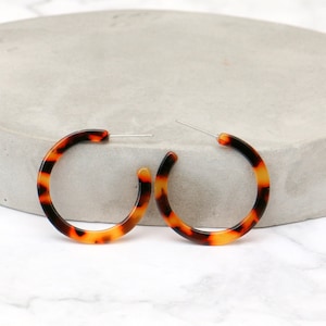 May include: A pair of tortoiseshell hoop earrings. The earrings are made of a thick, round plastic with a brown and orange pattern.