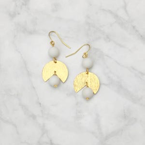 May include: Gold and white geometric earrings with two white beads and a gold crescent moon shape.