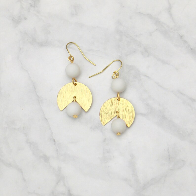 May include: Gold and white geometric earrings with two white beads and a gold crescent moon shape.