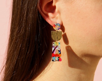 May include: Gold and multi-colored geometric dangle earrings. The earrings feature a small round top piece, a gold crescent shape, and a rectangular piece with a colorful abstract design.