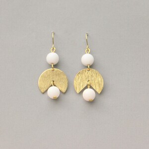 May include: Gold earrings with white beads and a geometric design. The earrings are made of gold metal and have a brushed finish.