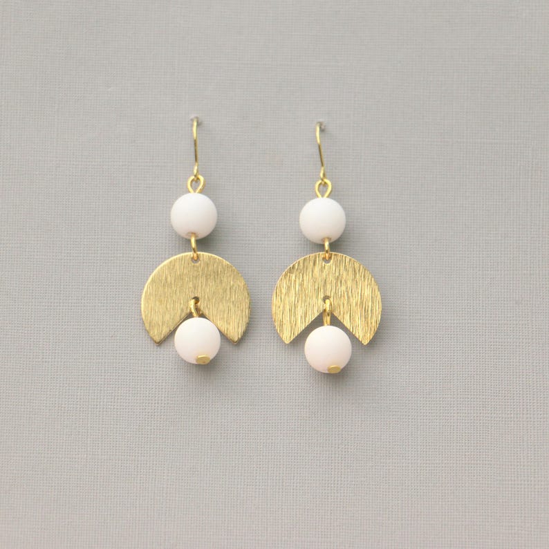 May include: Gold earrings with white beads and a geometric design. The earrings are made of gold metal and have a brushed finish.