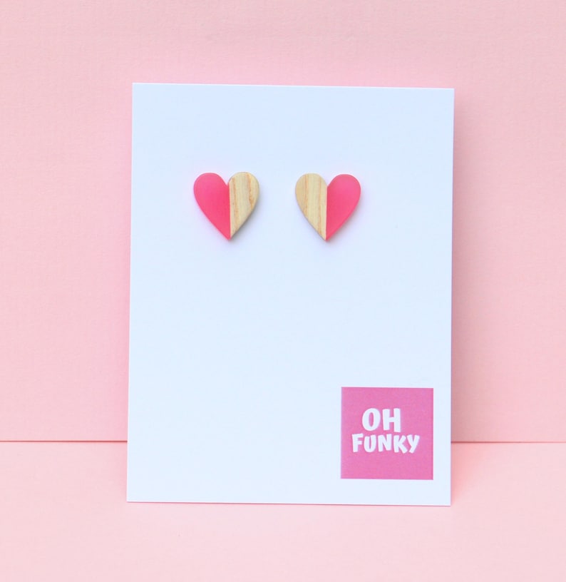 May include: A pair of pink and wood heart shaped stud earrings. The earrings are half pink and half wood. The earrings are on a white card with the text "OH FUNKY" in pink.