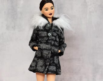 May include: A doll wearing a gray and black plaid coat with a white faux fur collar. The coat is buttoned and has pockets. The doll has dark hair and is wearing lipstick. The Etsy shop name "AmareDolls.etsy.com" is in the top right corner.