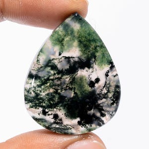 Pode incluir: Uma pedra preciosa de ágata musgo em forma de gota. A pedra apresenta uma base translúcida com padrões intrincados de inclusões verdes, pretas e brancas, assemelhando-se a uma paisagem em miniatura. A superfície polida reflete a luz.