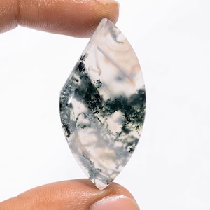 May include: A polished, teardrop-shaped gemstone with a translucent, creamy white base. The stone features intricate patterns of dark green and gray inclusions, creating a natural, artistic design. The gemstone is held between two fingers.