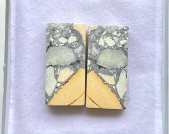 Puede incluir: Dos piezas de piedra rectangulares con un patrón único. La parte superior presenta una mezcla de gris, blanco y negro, mientras que la parte inferior es de color amarillo-beige. Las piedras se muestran en una caja blanca.