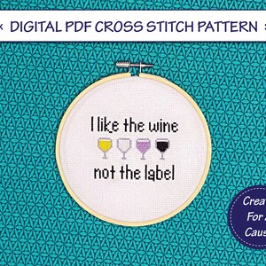 May include: Cross stitch pattern for a hoop with the text "I like the wine not the label" and four wine glasses in different colors. The pattern is on a white background and the hoop is on a teal background.