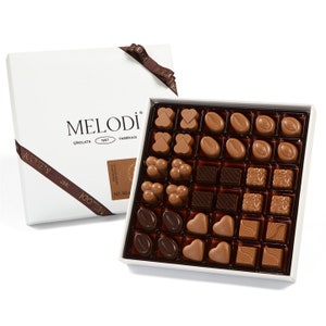 May include: A white box of assorted chocolates from Melodi Çikolata Fabrikası, a Turkish chocolate company established in 1967. The box contains a variety of milk and dark chocolate pieces in different shapes, including hearts, squares, and coffee beans.