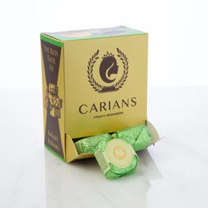 May include: A box of Kataifi Kunafa chocolates from Carians, elegant chocolatier. The box is gold with a brown and green design and the text "The Rich Taste Of". Several individually wrapped chocolates are visible.